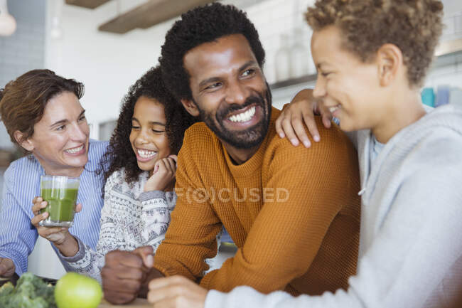 Sonriente familia multiétnica bebiendo batido verde saludable en la cocina - foto de stock