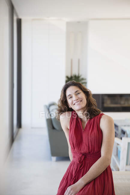 Portrait femme brune souriante et confiante en robe rouge à la maison — Photo de stock