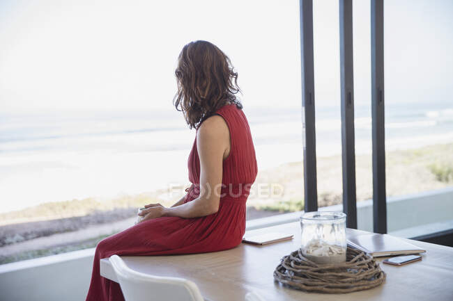 Pensive, ruhige brünette Frau, die vom Esstisch auf den Ozean blickt — Stockfoto