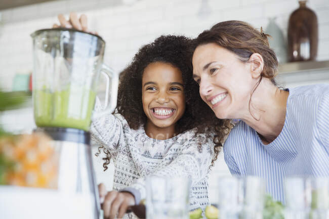 Sorrindo, mãe entusiasmada e filha fazendo smoothie verde saudável no liquidificador na cozinha — Fotografia de Stock