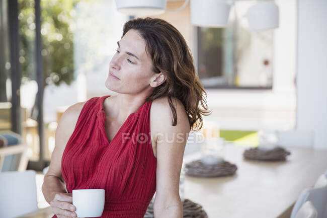 Pensive brunette woman drinking coffee in dining room, looking away — Stock Photo