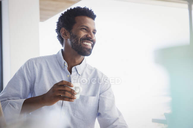 Sorrindo, homem entusiasta bebendo café e olhando para longe — Fotografia de Stock