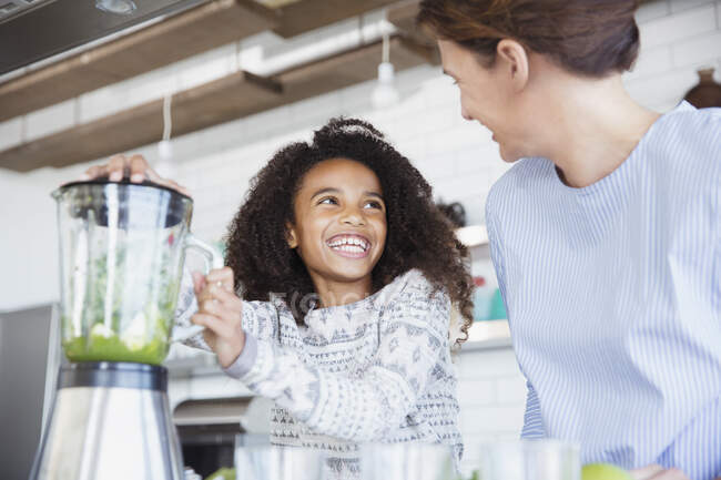 Filha entusiasmada ajudando a mãe a fazer smoothie verde saudável no liquidificador na cozinha — Fotografia de Stock