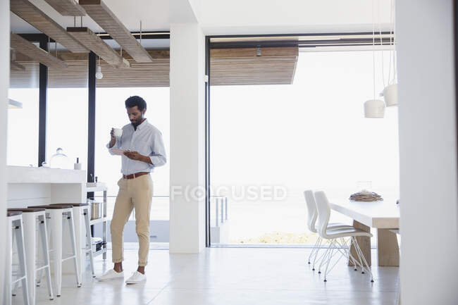 Businessman drinking coffee and using digital tablet in kitchen — Stock Photo