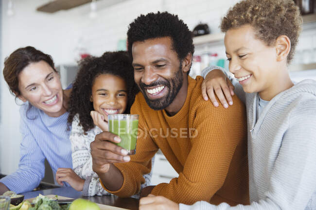Familia multiétnica bebiendo batido verde saludable en la cocina - foto de stock