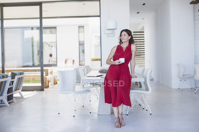 Retrato mulher morena confiante em vestido vermelho beber café na sala de jantar — Fotografia de Stock