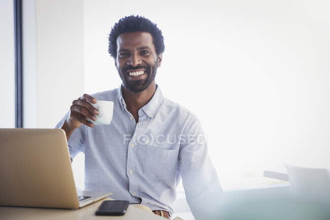Portrait smiling, confident businessman drinking coffee at laptop — Stock Photo