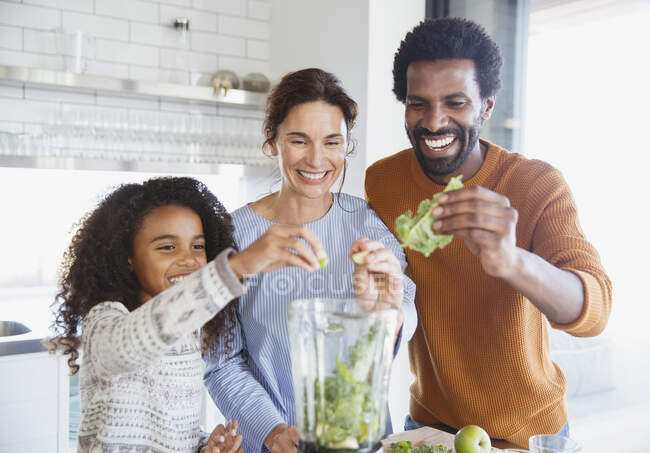 Smiling multi-ethnic family making green smoothie in blender in kitchen — Stock Photo