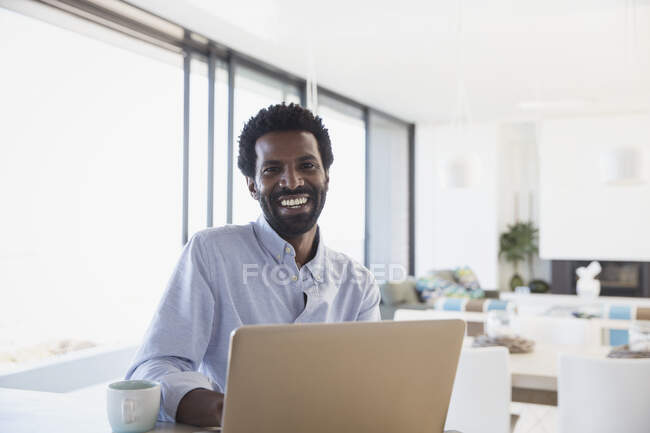 Portrait homme d'affaires souriant et enthousiaste buvant du café, travaillant à l'ordinateur portable dans la cuisine — Photo de stock