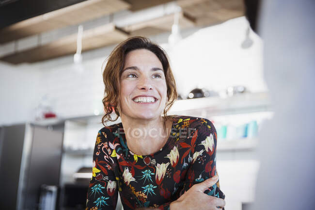 Mujer morena sonriente escuchando, mirando hacia otro lado en la cocina - foto de stock