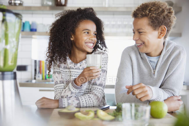 Sorrindo irmão e irmã bebendo smoothie verde saudável na cozinha — Fotografia de Stock