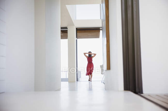 Mujer de pie con las manos detrás de la cabeza en el pasillo de casa - foto de stock