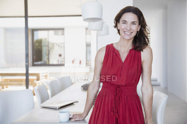 Retrato sorrindo, mulher morena confiante em vestido vermelho na sala de jantar — Fotografia de Stock