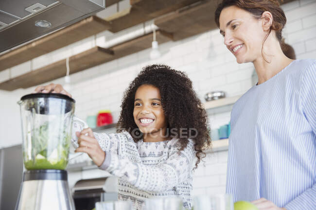 Мать и дочь делают здоровый зеленый смузи в блендере на кухне — стоковое фото