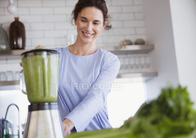 Smiling woman making healthy green smoothie in blender in kitchen — Stock Photo