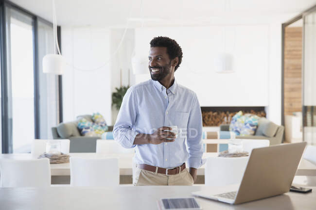Empresário sorrindo bebendo café no laptop na cozinha — Fotografia de Stock