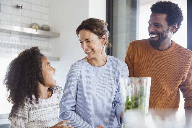 Familia multiétnica haciendo batido verde saludable en la licuadora en la cocina - foto de stock
