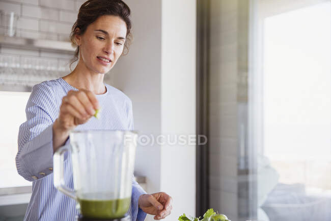 Woman making healthy green smoothie in blender in kitchen — Stock Photo