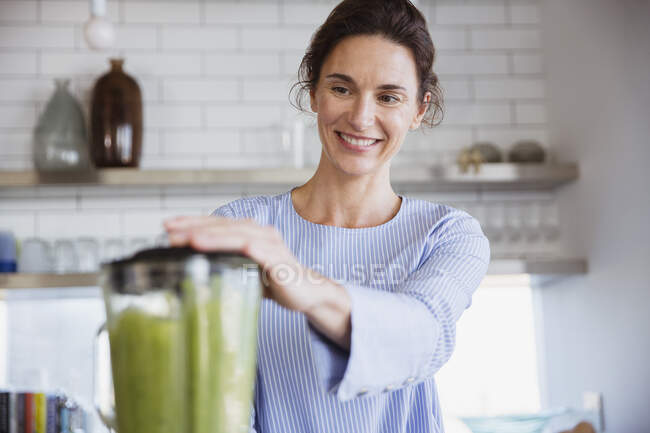 Sorrindo mulher fazendo saudável smoothie verde na cozinha — Fotografia de Stock