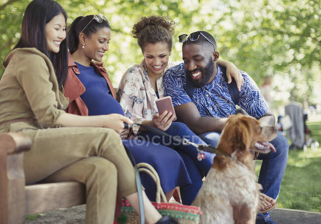Smiling friends with dog using smart phone in park — Stock Photo