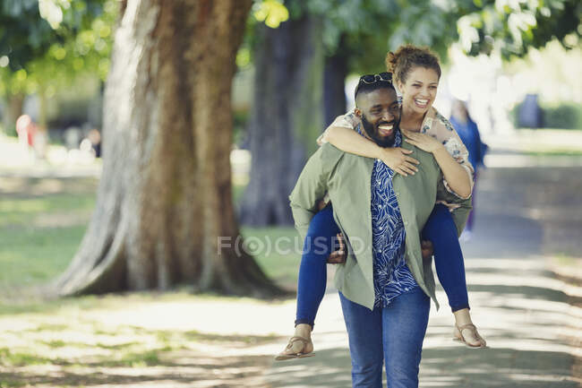 Jeune couple ludique piggybackking dans le parc — Photo de stock
