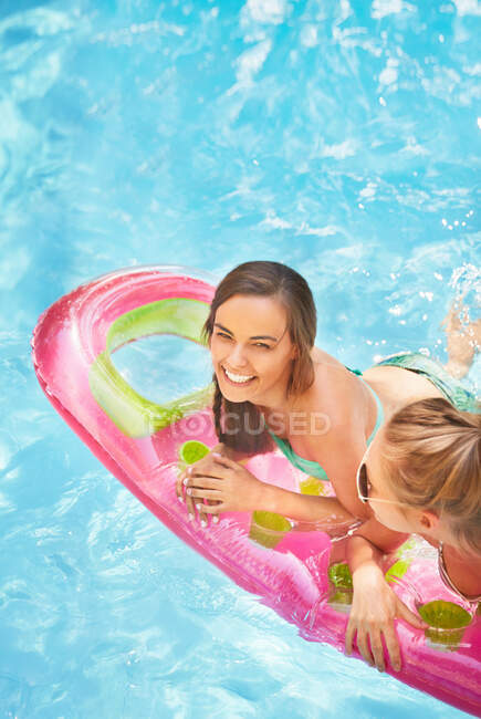 Портрет улыбающихся женщин-друзей, плавающих на плоту в бассейне летом — стоковое фото