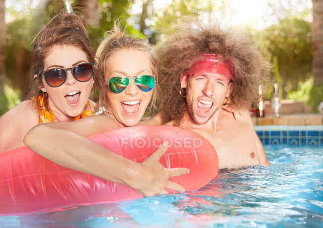 Ritratto esuberante, giocoso giovani amici con zattera gonfiabile in piscina estiva — Foto stock