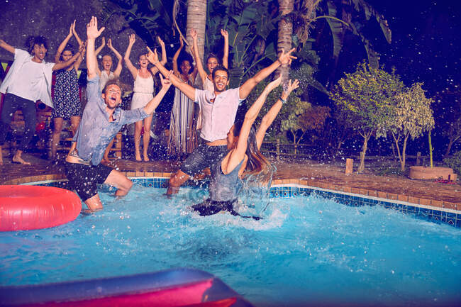 Portrait exuberant young friends jumping into swimming pool at night — Stock Photo