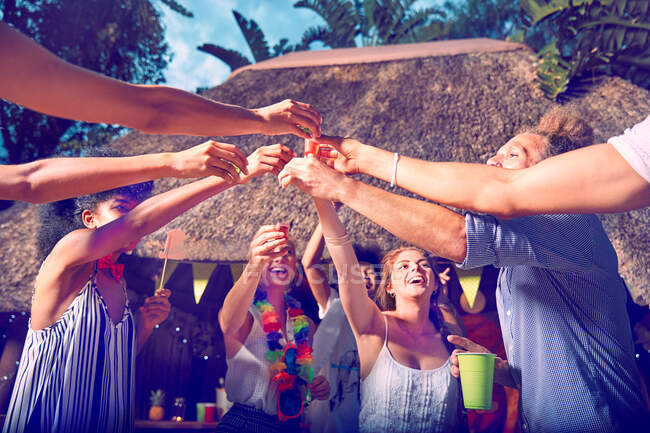 Jóvenes amigos brindando por el alcohol en vasos de chupito en la fiesta junto a la piscina - foto de stock