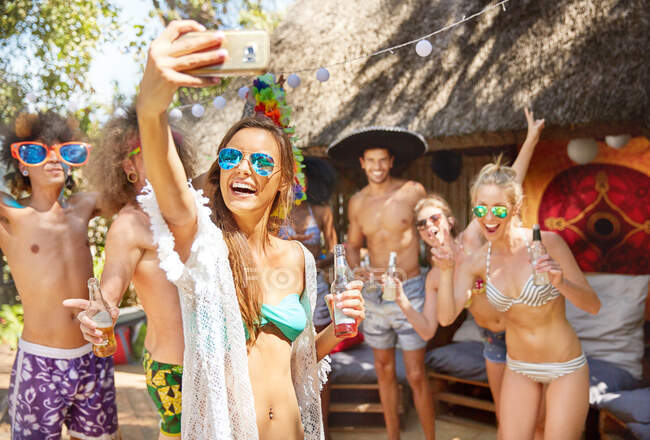 Enthusiastic young friends drinking and taking selfie at sunny summer poolside party — Stock Photo