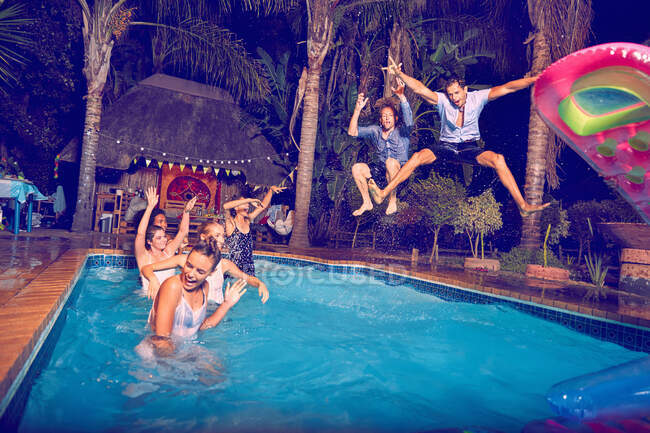 Exuberant young men friends jumping into swimming pool at night — Stock Photo