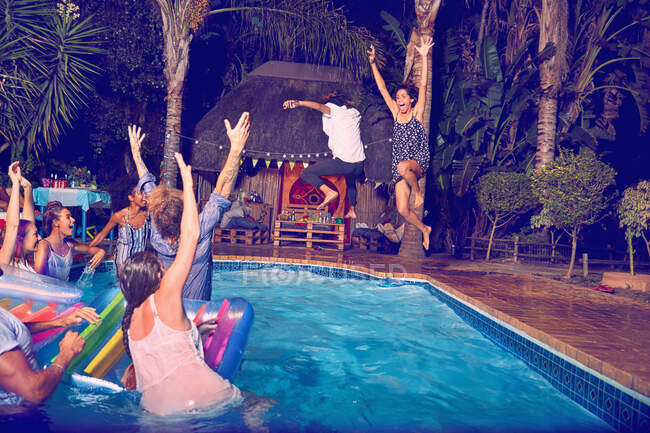 Young friends playing, jumping into swimming pool at night — Stock Photo
