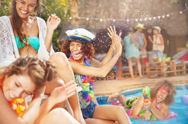 Jovem com pistola de ejaculação pulverizando mulheres amigas na piscina de verão — Fotografia de Stock