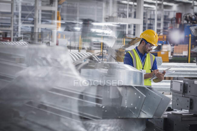 Trabalhador da fábrica com prancheta inspecionando peças de aço na fábrica — Fotografia de Stock