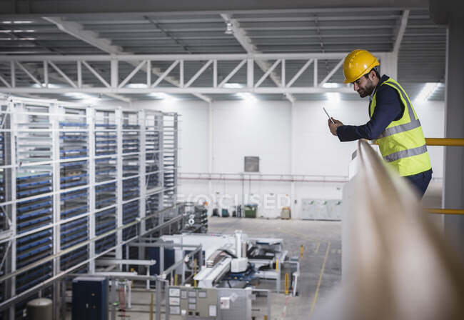 Мужчина-супервайзер с планшетом на платформе, смотрит вниз на фабрику — стоковое фото