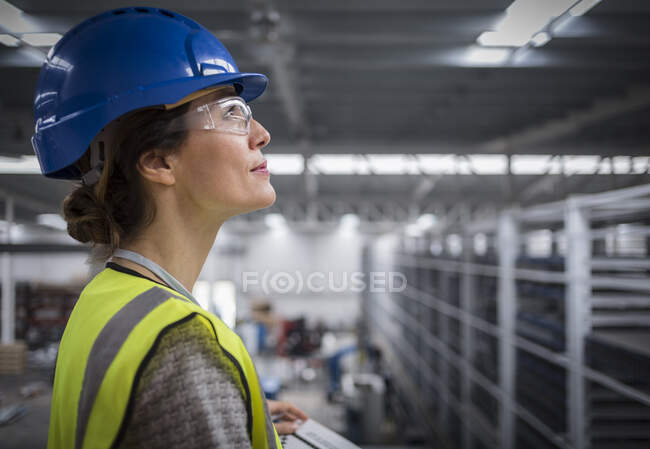 Sorrindo, confiante supervisor feminino em chapéu duro olhando para cima na fábrica — Fotografia de Stock