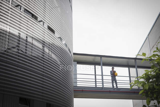 Female supervisor standing on elevated walkway between factory buildings — Stock Photo
