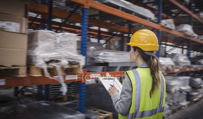 Female factory worker with clipboard checking inventory in warehouse — Stock Photo