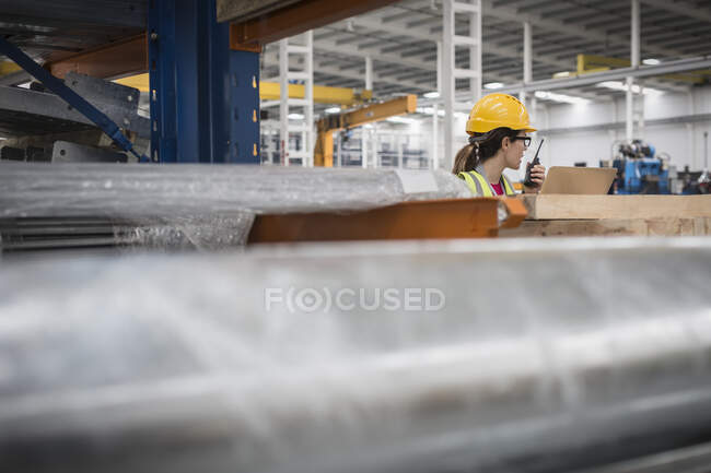 Женщина-работница ноутбука разговаривает по рации на заводе — стоковое фото