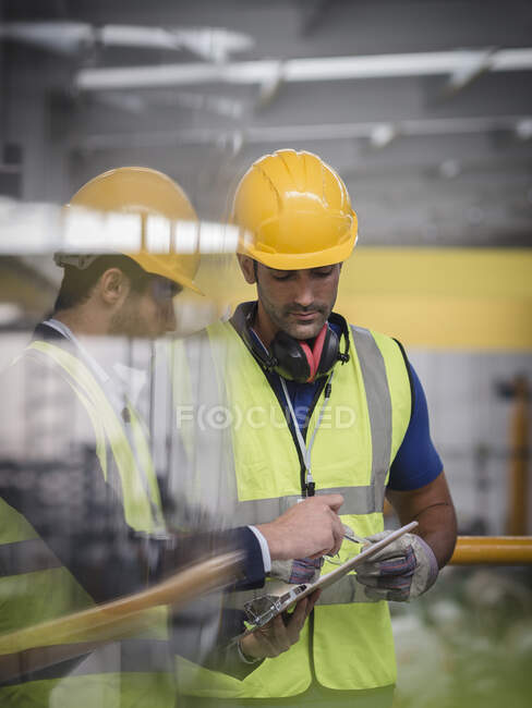 Männlicher Vorgesetzter und Arbeiter mit Klemmbrett im Gespräch in Fabrik — Stockfoto