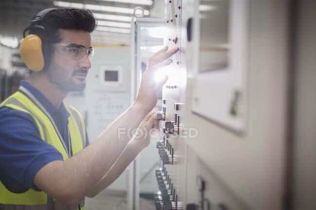 Male worker wearing ear protectors, operating machinery at control panel in factory — Stock Photo