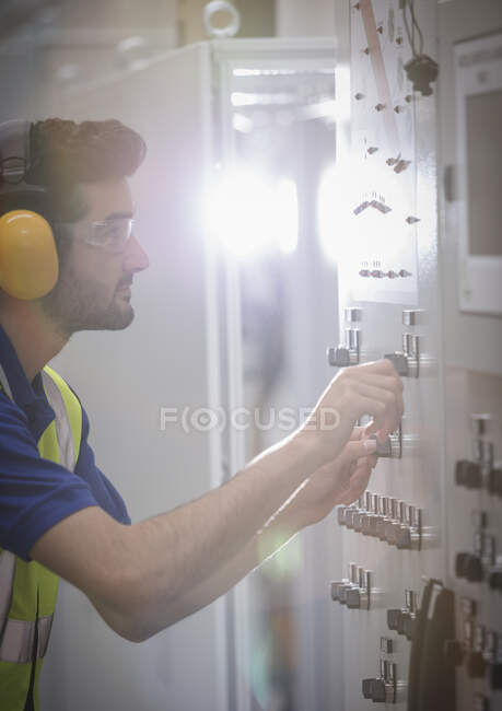 Travailleur masculin portant des protecteurs d'oreille, utilisant des machines au panneau de commande dans l'usine — Photo de stock