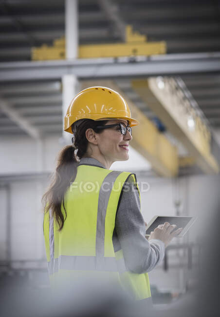 Selbstbewusste, lächelnde Arbeiterin nutzt digitales Tablet in Fabrik — Stockfoto