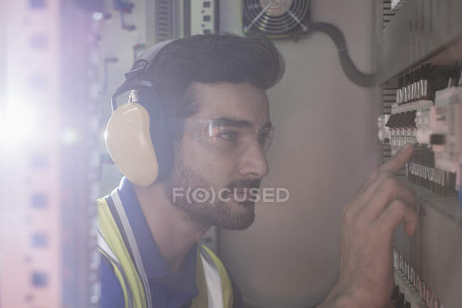 Серьезный работник мужского пола носит ушные протекторы, работающие машины на панели управления на заводе — стоковое фото