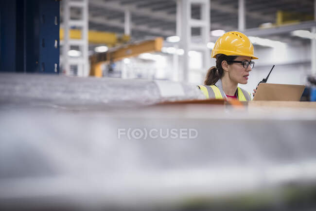 Trabalhadora feminina usando laptop e walkie-talkie na fábrica — Fotografia de Stock