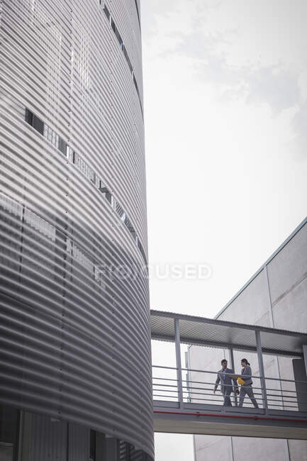 Наглядачі, що ходять по підвищеній доріжці між заводськими будівлями — стокове фото