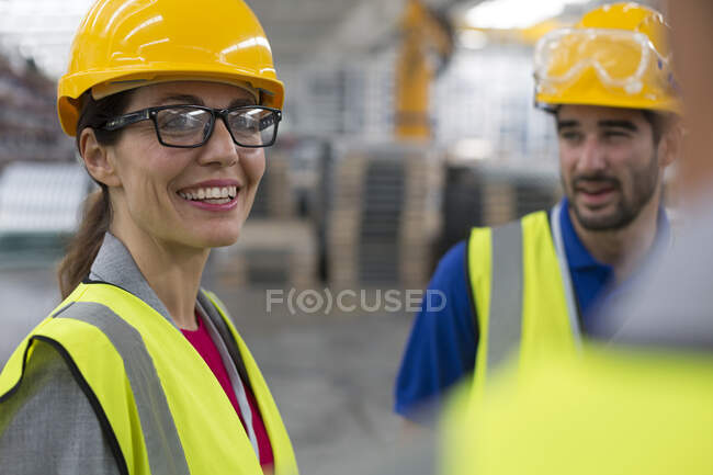 Trabajadora sonriente hablando con compañeros de trabajo en la fábrica - foto de stock