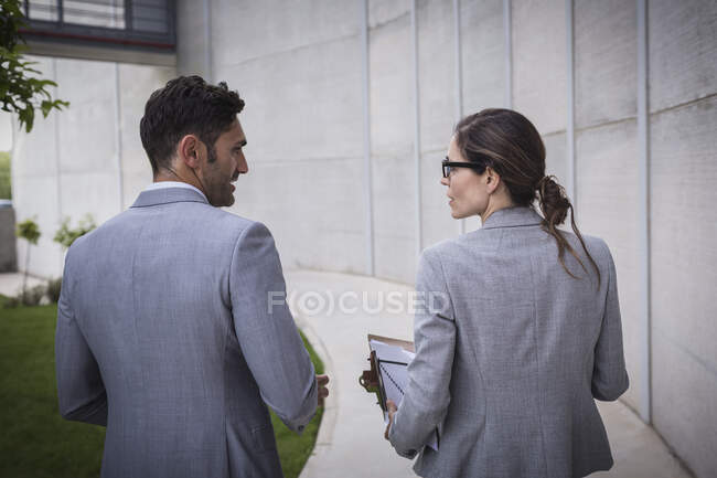 Businessman and businesswoman walking and talking on sidewalk — Stock Photo
