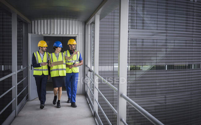 Supervisores con portapapeles caminando y hablando en la pasarela elevada fuera de la fábrica - foto de stock