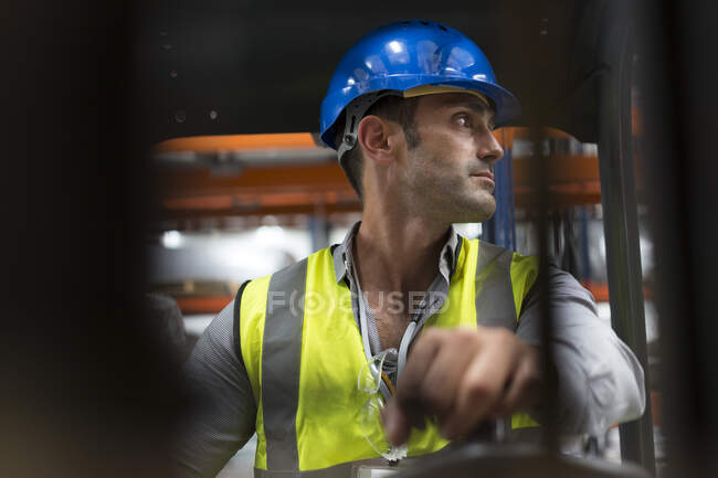 Male worker driving forklift, looking over shoulder in factory — Stock Photo
